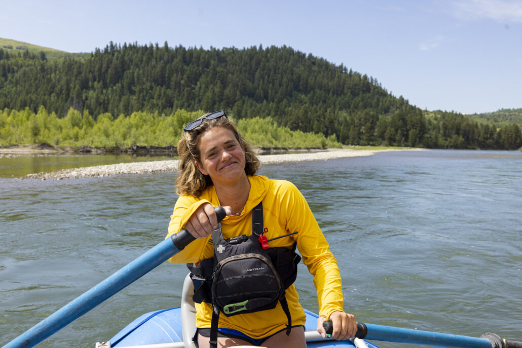 A happy rafting guide in a yellow shirt paddles down the scenic Snake River.