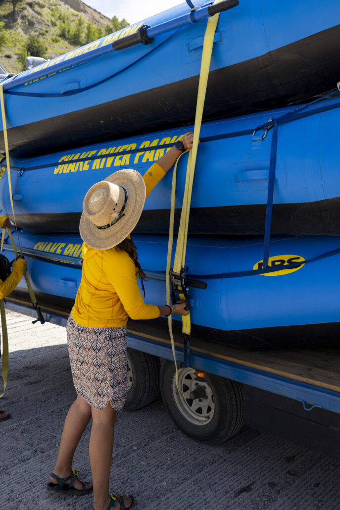 A rafting guide secures three inflatable blue rafts onto a trailer.