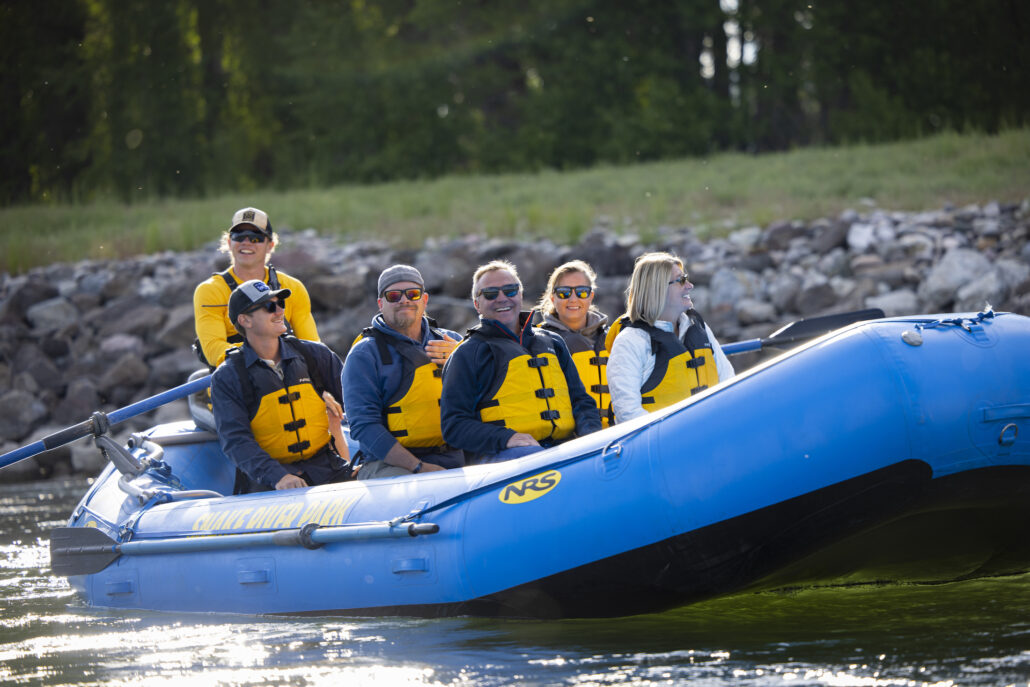 A group of adults smiling for the camera as they float down the Snake River on a scenic rafting trip.